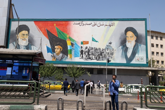 Iranians walk past a billboard bearing the portraits of Iran's Supreme Leader Ayatollah Ali Khamenei (L) and late supreme leader Ayatollah Ruhollah Khomeini in the capital Tehran on August 13, 2022. (Getty Images)  
